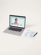 Laptop showing a video consultation with a clinician, next to a printed report.